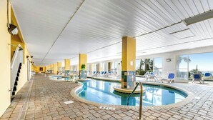 An indoor swimming pool with a tiled floor, lounge chairs, and a view of the outside. - Camelot by the Sea 0809 (Myrtle Beach)
