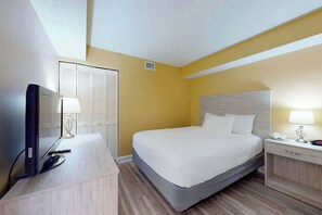 A hotel room with a bed, bedside table, lamp, TV, and a wardrobe. - Camelot by the Sea 0809 (Myrtle Beach)