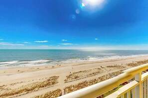 A beach with a clear sky, a sandy shore, and a railing in the foreground. - Camelot by the Sea 0809 (Myrtle Beach)