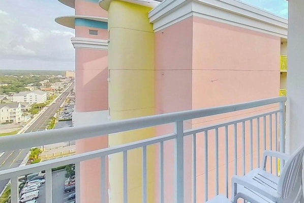 A balcony with a railing, a view of a cityscape, and a building with a pink and yellow facade. - Bay Watch Resort 1931 (North Myrtle Beach)