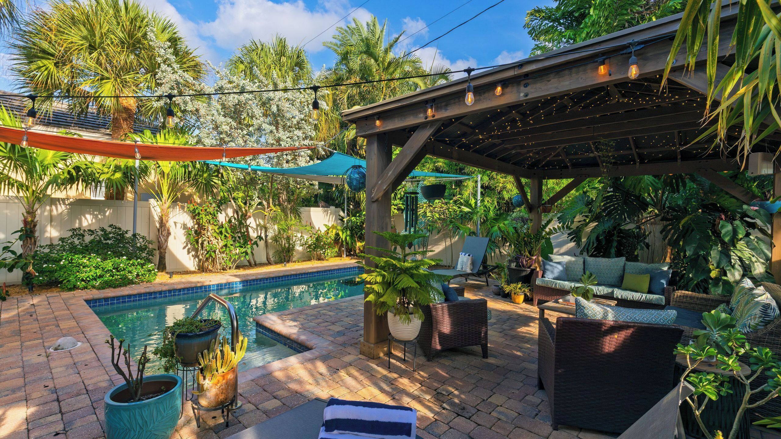 A backyard with a pool, outdoor furniture, and a pergola with string lights.