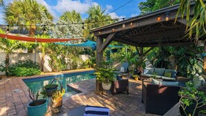 En baghave med swimmingpool, udendørs møbler og en pergola med lyskæder.
