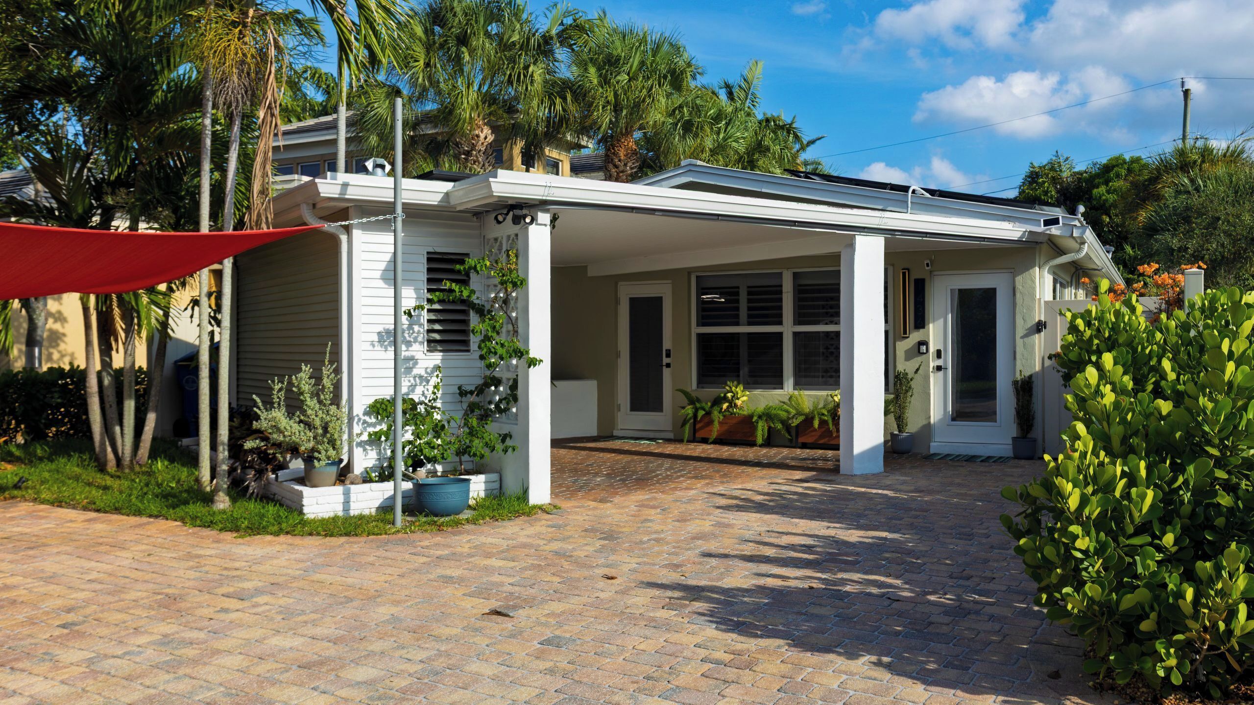 A house with a covered porch, a brick driveway, and various potted plants.