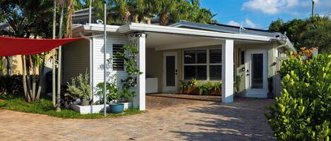 A house with a covered porch, a brick driveway, and various potted plants.