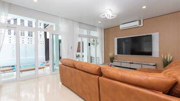 Una sala de estar moderna con un sofá de cuero, un televisor de pantalla plana montado en una pared de madera, y amplios ventanales correderos que dan a un espacio exterior.