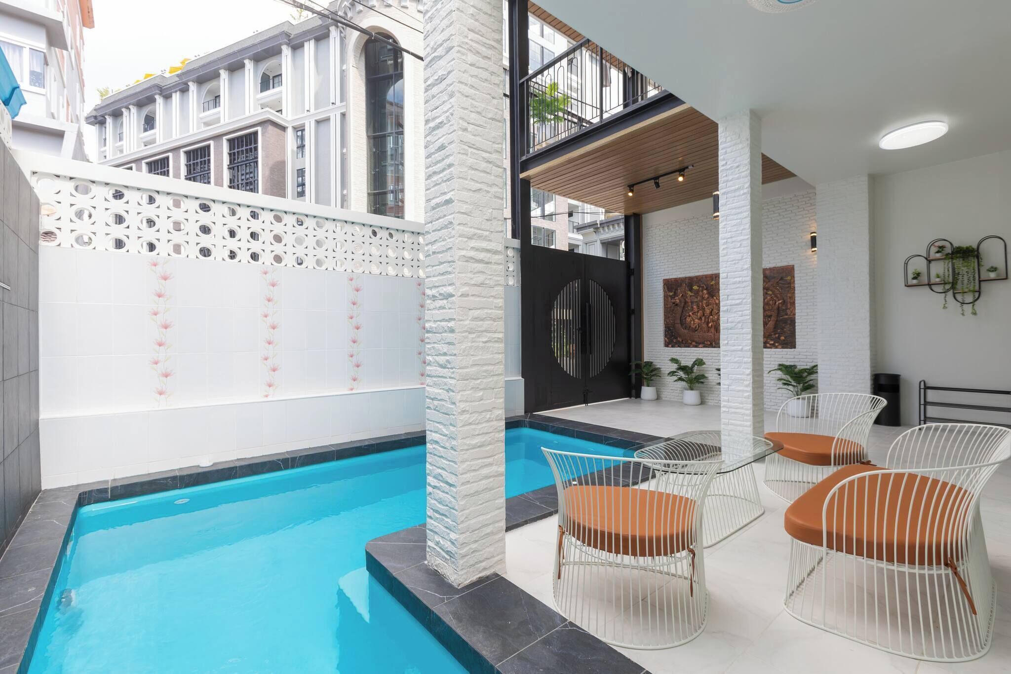 Un área de piscina interior moderna con una piscina azul cristalina, paredes blancas y un balcón con vistas a los edificios circundantes.