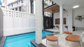 Un área de piscina interior moderna con una piscina azul cristalina, paredes blancas y un balcón con vistas a los edificios circundantes.