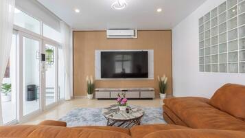 Una sala de estar moderna con un televisor de pantalla plana grande, un conjunto de sofás y una mesa de centro con un jarrón de flores.