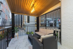 A balcony with wicker furniture, a potted plant, and a view of a building with a sign. - Luxury4br Pool Villawalk to Patongbeachrooftop BBQ (Patong)