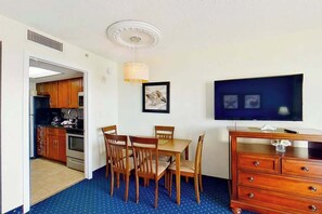 A room with a dining table, chairs, a television, a dresser, and a kitchen area visible through an open doorway. - Bay Watch Resort 1936 (North Myrtle Beach)