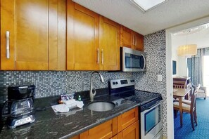 A kitchen with wooden cabinets, a microwave, a stove, and a coffee maker. - Bay Watch Resort 1936 (North Myrtle Beach)