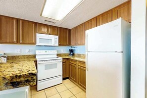 Une cuisine avec des meubles de rangement en bois, un réfrigérateur blanc, un four à micro-ondes et une cuisinière.