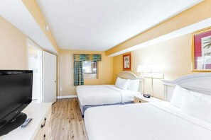 A hotel room with a TV, two beds, a bedside table, a lamp, and a window with curtains. - Camelot by the Sea 0211 (Myrtle Beach)