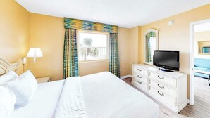 Quarto de hotel com uma cama, televisão, penteadeira e janela com cortinas.