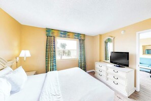 Ein Hotelzimmer mit einem Bett, einem Fernseher, einem Schminktisch und einem Fenster mit Vorhängen.