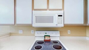 Une cuisine avec un four à micro-ondes placé au-dessus d’une cuisinière, des placards au-dessus du four à micro-ondes et une petite boîte sur la cuisinière.