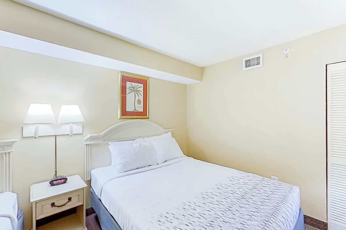 Een hotelkamer met een eenpersoonsbed, een nachtkastje met een lamp, een aan de muur hangend schilderij en een raam met jaloezieën.