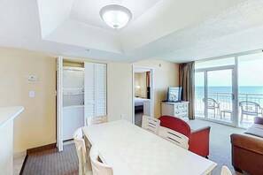 Ein Hotelzimmer mit Essbereich, Kleiderschrank, Fernseher und einem Balkon mit Meerblick.