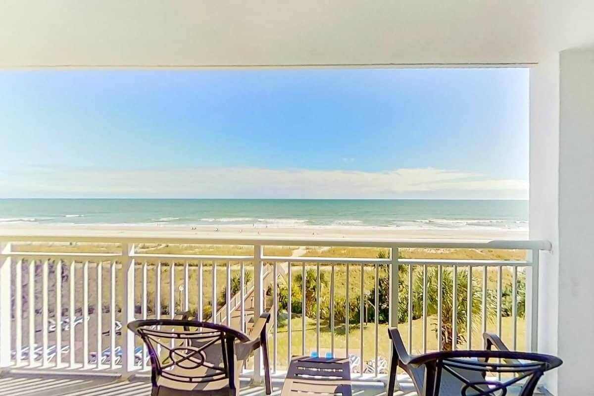 A balcony with a view of the beach, equipped with chairs and a table.