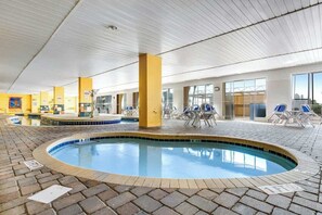 Une piscine intérieure avec un sol carrelé, des chaises longues et un plafond orné d’un motif en réseau.
