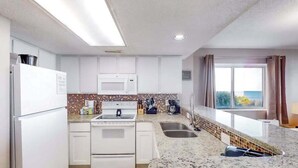 Eine moderne Küche mit weißen Schränken, einer Granitabdeckung, einem eingebauten Backofen und einem Fenster mit Vorhängen.