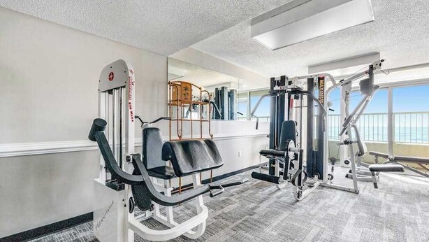 Ein Fitnessraum mit Trainingsgeräten, einem Spiegel und Blick ins Freie.