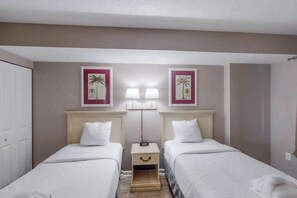 Une chambre d’hôtel avec deux lits simples, une table de chevet avec une lampe et deux tableaux encadrés au mur.