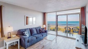 Ein Zimmer mit einer Couch, einem kleinen Tisch, einem Fernseher und einem Balkon mit Meerblick.