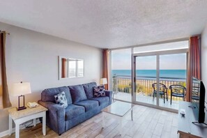 A room with a sofa, a small table, a TV, and a balcony with a view of the sea. - Camelot by the Sea 0317 (Myrtle Beach)
