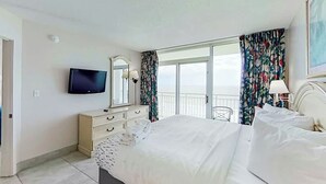 Habitació d'hotel amb llit, televisió, prestatge i balcó amb cortines.