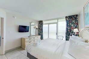 Ein Hotelzimmer mit Bett, Fernseher, Schminktisch und einem Balkon mit Vorhängen.