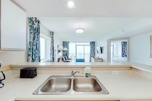 A modern kitchen with a double sink, a toaster, and a mirror reflecting the room. - Camelot by the Sea 0817 (Myrtle Beach)