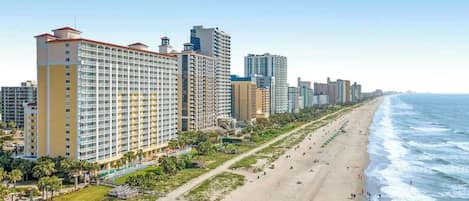 A beachfront hotel with multiple high-rise buildings, a sandy beach, and a clear view of the ocean.