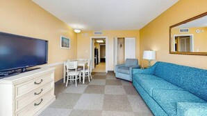 Ein Hotelzimmer mit Fernseher, einem Esstisch mit Stühlen, einer Couch und einem Spiegel.