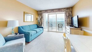 Ein Hotelzimmer mit einer Couch, einem Fernseher, einem Esstisch und einem Balkon mit Blick.