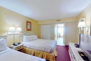 A hotel room with a bed, bedside tables, lamps, a television, and a door leading to another room. - Camelot by the Sea 0516 (Myrtle Beach)