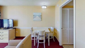 A compact room with a dining table, chairs, a television, and a closet. - Camelot by the Sea 0516 (Myrtle Beach)