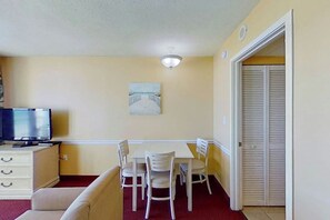 Ein gemütlicher Raum mit Esstisch, Stühlen, Fernseher und Kleiderschrank.