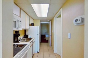 Een smalle gang met een kitchenette aan de linkerkant, een magnetron, een koffiezetapparaat en een koelkast. Een digitale thermostaat is aan de rechterkant aan de muur bevestigd.