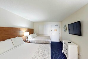 A hotel room with two beds, a TV, a dresser, and a door leading to another room. - Camelot by the Sea 1102 (Myrtle Beach)