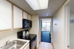 Een compacte keuken met een magnetron, fornuis en spoelbak. Door de deur is een balkon met uitzicht zichtbaar.