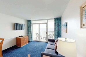 Een hotelkamer met een flatscreen televisie, een bank, een bureau met lades, een lamp en een balkon met stoelen.