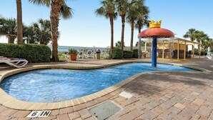 A swimming pool with a 6-inch depth marker, surrounded by palm trees and a gazebo with a crown-shaped water feature. - Camelot by the Sea 0617 (Myrtle Beach)