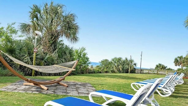 A row of sun loungers with blue cushions, a hammock, and palm trees in the background. - Camelot by the Sea 0617 (Myrtle Beach)