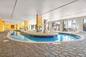 Uma piscina interior com borda azulejada, uma fonte central e chão de tijolos.