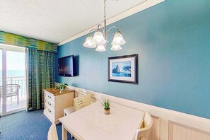 Um quarto com uma mesa de jantar, cadeiras, uma televisão, um quadro e uma planta.