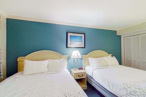 A hotel room with two beds, a nightstand with a lamp, a framed picture on the wall, and a closet. - Camelot by the Sea 1016 (Myrtle Beach)