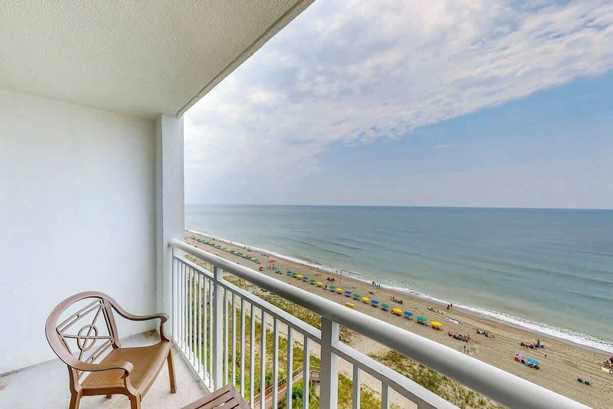 Un balcon donnant sur une plage, un banc en bois et une rambarde.