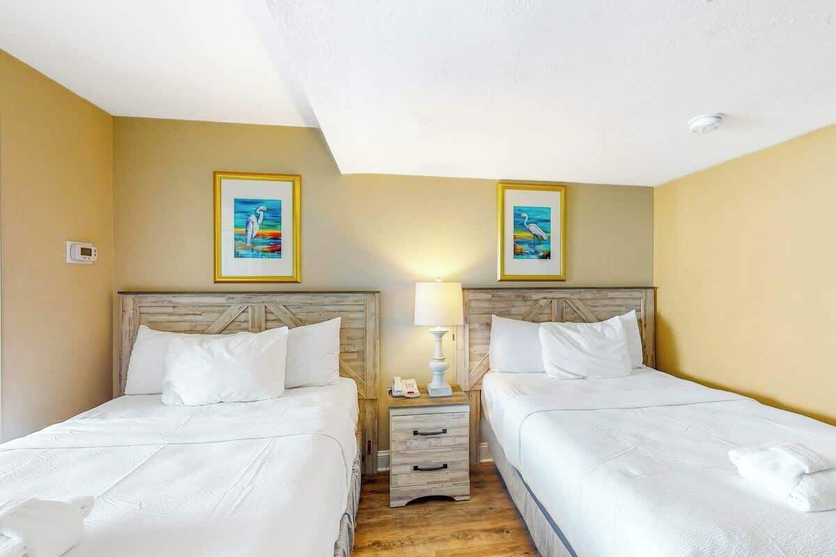 Ein Hotelzimmer mit zwei Betten, einem Nachttisch mit Lampe sowie zwei gerahmten Bildern an der Wand.