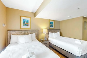 A hotel room with two beds, a wooden headboard, a nightstand with a lamp, and framed artwork on the wall. - Camelot by the Sea 1103 (Myrtle Beach)